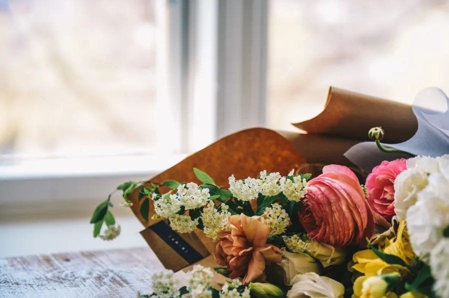 Bouquet de fleurs fraîches emballé dans du papier kraft posé sur une table en bois